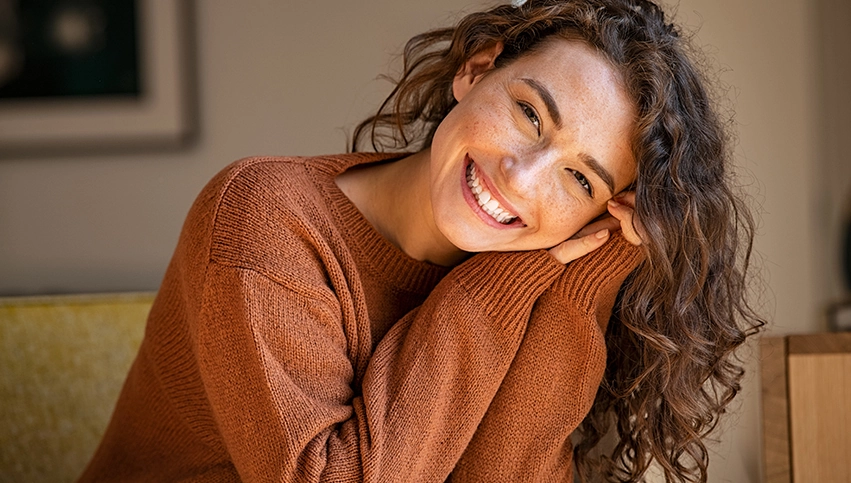 Woman with orange sweater on, smiling at the camera